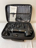 Photo showing open carrying case containing CARECI black massage gun, six different massage heads, instruction manual, and charging cable.
