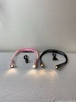 Two neck lights displayed on a flat surface, one pink with protective wrapping and one black, both lit showing LED illumination with USB cables beside them.