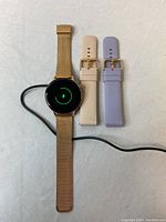 I39H Smart Watch with gold metal mesh strap attached shown charging on a cloth background, screen shows charging symbol.