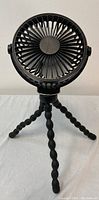 Front view of black mini fan with flexible tripod legs standing on a surface.
