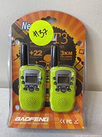 Front view of BaoFeng T3 walkie talkie set in sealed packaging showing two lime green radios and product details such as channel count and call range.