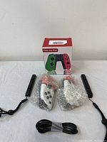 Two Elite Joy-Pad gaming controllers in bubble wrap with wrist straps and charging cable on white surface, boxed behind.