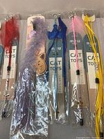 Photo showing 8 brand new cat sticks in packaging with various feathered and decorative attachments.