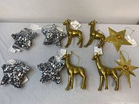 Top view of 10 assorted Christmas ornaments: 4 silver sequinned stars, 4 gold giraffes, 2 gold stars displayed on flat surface