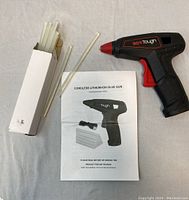 Workbench view of the cordless WerkTough glue gun, user manual, and box of glue sticks arranged on a cloth.