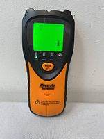 Front view of the Mecurate stud finder showing the LCD screen on and the stud mode activated.