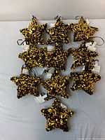 Ten gold star-shaped Christmas ornaments covered with shiny sequins laid out on a flat surface, front view showing texture and shape.