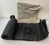 Black perforated grounding mat partially folded with attached black cable and beige storage pouch behind it.