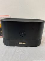 Front view of black LED flame diffuser showing steam symbol and control buttons.