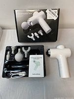 Complete fascial massage gun set in packaging including device, four massage heads, USB cable, and manual