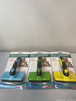 Three self-cleaning slicker pet brushes in original packaging with blue, green, and yellow handles.