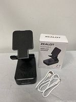 Photo showing Zealot Z7 speaker and phone holder device with USB charging cable next to original product box.