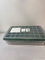 Long side view of the sealed seedling starter kit box featuring a green seed tray with numerous cells and a clear plastic lid under shrink wrap.