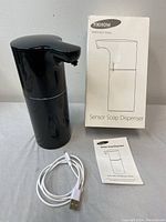 Black YikHom YKH7402 sensor soap dispenser alongside its box and USB charging cable on a white surface.