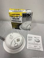 Photo of BRK SC9120BA alarm with box and user manual displayed, showing front and product details.