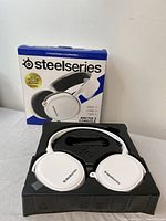 Box of SteelSeries Arctis 3 Console headset shown along with the headset itself in packaging tray. White color with black ear cushions visible.