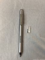 Silver Huawei stylus pen with clip and two replacement tips in plastic bag on gray fabric.