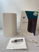 Front view of the white WIELOV True HEPA Air Purifier P100 Mini alongside its box and instruction manual.