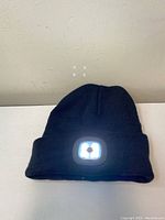 Front view of black knit toque showing rectangular LED light panel on cuff illuminated bright white.