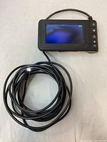 Endoscope with flexible cable coiled and LED camera tip visible, device screen off, control buttons visible on side.