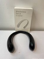 Front view of black U-shaped bladeless neck cooler with original white packaging box showing product image and name.