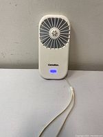Front view of white Camelion handheld mini fan showing circular fan blade grille, brand name, and blue LED indicator lights.