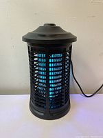 Front angle showing the mosquito killer lamp with blue UV light turned on and protective black grid.