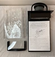 Top view showing the tall textured glass panel, instructions sheet, and short glass panel piece beside the black mounting bracket.