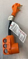 Full view of orange RV adapter cable showing 50 amp male plug and 30 amp female end with molded handles and attached safety and usage tags.