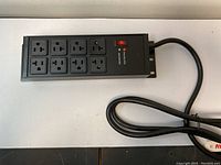 Top view of black power strip showing 8 outlets and red indicator lights for protection and power.