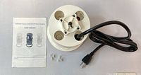White pop-up outlet showing AC sockets, power cord, instruction manual, and installation parts.