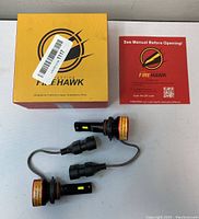 Firehawk branded yellow packaging box with two LED bulbs and an instruction manual booklet on a white surface.