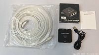 Photo of the Ethernet bundle including the coiled white Cat 6 flat cable, the ethernet splitter, USB power cable, splitter box and user manual.