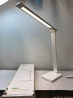 Side view of white LED desk lamp turned on, showing lamp head and arm fully extended with warm light emitted