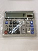 Full view of the calculator covered in plastic packaging showing the display and keypad layout.