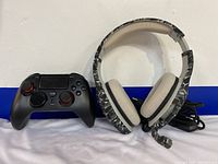 Photo showing black wireless controller with red ringed analog sticks beside wired camouflage pattern headset with thick padding and attached microphone.