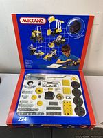 Photo of open box showing the organized metal parts, wheels, and motor inside a plastic tray. The tray contains yellow and silver perforated plates, wheels, and mechanical parts.