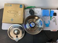 Full view of all parts including stainless steel fountain bowl, lid, power adapter, blue replacement filters, cleaning brushes, user manual, and additional small components.