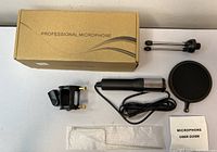 Photo of all items in the lot arranged on surface: cardboard box, microphone, microphone holder mount, pop filter, and user guide booklet