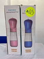 Two boxed portable dog water bottles, one pink and one blue, with labels showing water and food capacities on front.