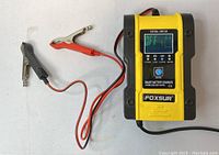 Photo showing the Foxsur smart battery charger, yellow and black body with red and black alligator clamp cables attached, digital LCD screen on display.