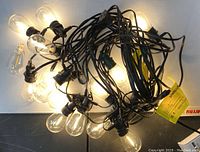 String lights lit up on white surface showing clear glass bulbs and black wiring.