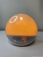 Photo of Ecozy wake up light alarm clock showing orange light on dome and digital display reading '30'.