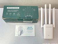 WiFi Range Extender with four antennas, quick manual, and packaging box arranged on a flat surface.