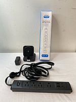 Photo showing TROND Prime II surge protector power strip with power cord, USB ports, wireless charging stand and its charger, and the power strip in front of a plain wall.