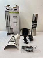 Photo of the electric wine opener set, including original box, charging base, power adapter, foil cutter in plastic, and user manual on a floor surface.
