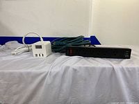 Black power strip, white cube power strip, and green coiled extension cord shown together on a white cloth.