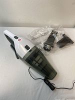 Front view of the handheld vacuum cleaner with two black accessories in sealed plastic packaging.