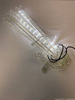 Icicle string light tubes bundled with clear wiring and power cord, illuminated showing LED lights inside clear tubes.