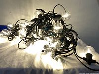 Tangled string lights illuminated, showing multiple clear globe bulbs emitting a warm white light, connected with black wiring.